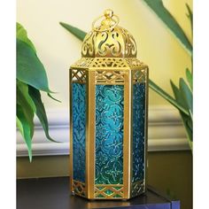 a blue and gold lantern sitting on top of a table next to a potted plant