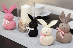 three small stuffed rabbits sitting on top of a table next to a candle and some rocks