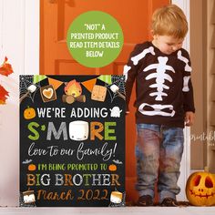 a young boy standing in front of a halloween sign with the words we're adding smore to our family