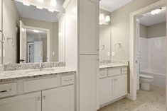 a bathroom with white cabinets and marble counter tops