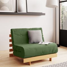 a green futon couch with pillows on it in front of a white wall and wooden floor