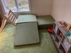 there is a bed with a green mattress on the floor next to a book shelf