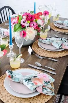 a table set with place settings and flowers in vases on the side, along with candles