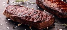 two steaks on a cutting board with herbs and seasoning around them for garnishes