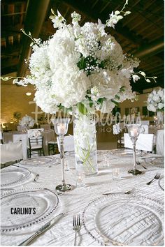 white flowers in a vase on a table with silverware and place settings for dinner