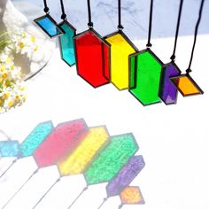 the sun shines brightly on colorful glass pieces hanging from black cords, with flowers in the background