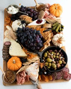 an assortment of cheeses, meats and vegetables on a cutting board with pumpkins