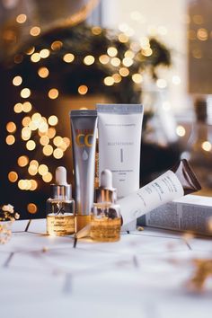 an assortment of skin care products sitting on a table next to a christmas tree with lights in the background