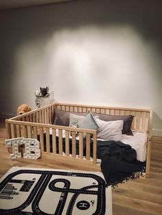 a wooden crib with pillows and blankets on the floor in front of a white wall