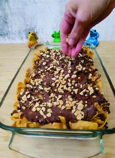 a person placing nuts on top of a chocolate covered pastry in a glass baking dish