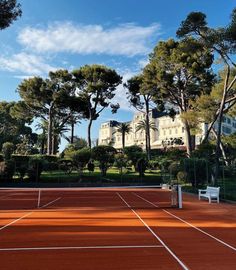 a tennis court surrounded by trees with a building in the background