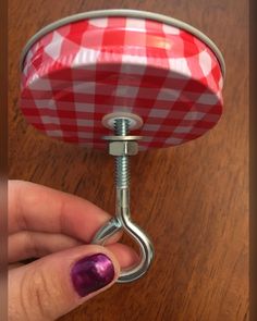 a hand holding a red and white checkered umbrella on a metal hook that is attached to a wooden table