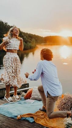 a man and woman dancing on a dock by the water at sunset, with one holding her leg up