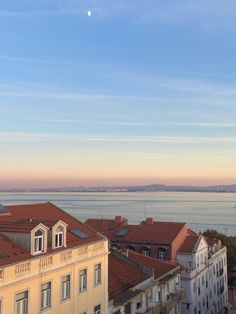 a view of some buildings and the ocean in the distance with a half moon above them