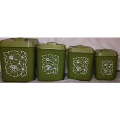 four green canisters with flower designs on them sitting next to each other in front of a white curtain