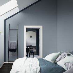 a bedroom with blue walls and white bedding in an atticed space that has a skylight above the bed