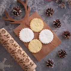 three cookies are on a cutting board next to some pine cones and a rolling pin