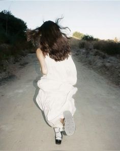 a woman walking down a dirt road with her hair blowing in the wind