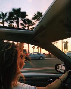 the woman is driving her car down the street at sunset or dawn, with palm trees in the background