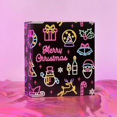 a black box with colorful christmas stickers all over it on a pink and purple background