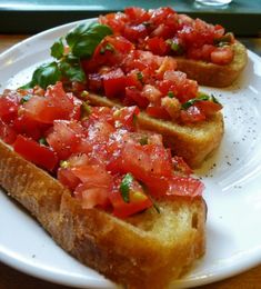 two pieces of bread with tomatoes and basil on them sitting on a plate next to a glass container