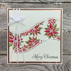 a merry christmas card with poinsettis and ribbon on the front, sitting on a wooden surface