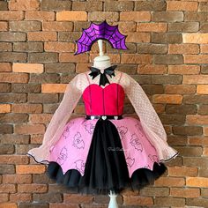 a pink and black dress with spider webs on the top, sitting against a brick wall