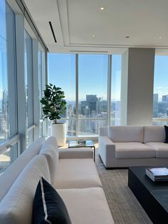 a living room filled with white furniture and tall windows overlooking the cityscape in the distance