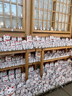 there are many white and red ceramic cats on display in the storefront window,