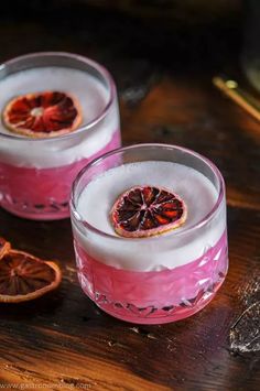 two glasses filled with blood oranges on top of a wooden table