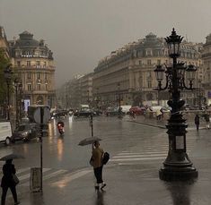 people walking in the rain with umbrellas on a city street near buildings and lamps