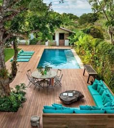 an outdoor patio with blue couches and tables next to a pool surrounded by trees