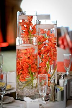 orange flowers are in glass vases on a table with silverware and wine glasses