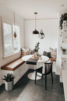 a kitchen with white walls and black flooring next to a dining room table surrounded by potted plants