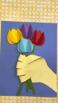 a hand holding flowers made out of paper on a blue background with yellow and red strips