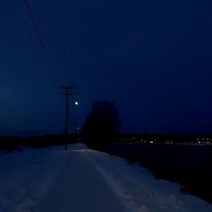 an empty road at night with power lines and telephone poles in the snow on either side