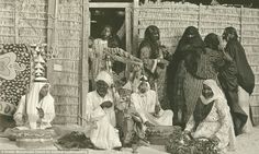 an old black and white photo of people in front of a hut with baskets on the floor