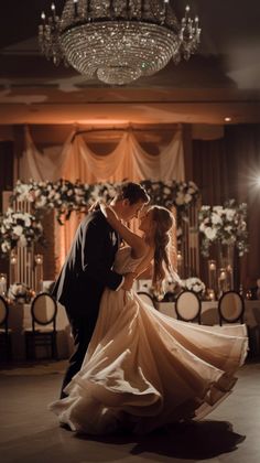 a bride and groom dance together in front of a chandelier at their wedding reception