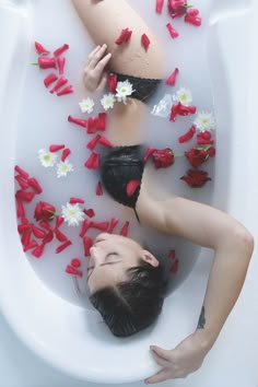 a woman in a bathtub with flowers floating on the water and petals scattered around her