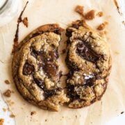 two chocolate chip cookies sitting on top of a table next to a jar of milk