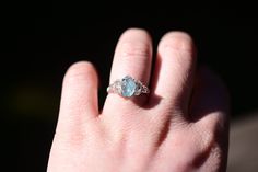 a person's hand with a ring on it that has a blue stone in the middle