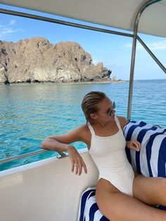 a woman sitting on the back of a boat in the ocean next to a rock formation