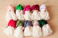 a group of christmas gnomes hanging from strings on a wooden table with one wearing a santa claus hat