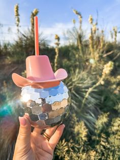 a person holding up a disco ball with a cowboy hat on it in front of some plants