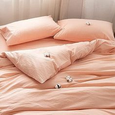 an unmade bed with peach colored sheets and pillows on it, in front of a window