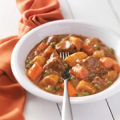 a white bowl filled with stew and carrots on top of a table next to a fork