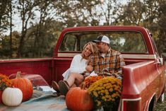 a man and woman sitting in the back of a truck with pumpkins on the bed