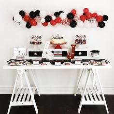 a white table topped with lots of cake next to red and black balloons on the wall