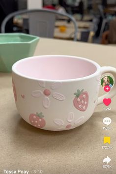 a pink and white cup sitting on top of a counter next to a green bowl