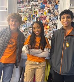 three young people standing next to each other in front of a wall with pictures on it